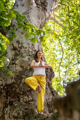 Beautiful woman with gorgeous curly hair doing yoga in nature, dressed in white and yellow combination, concept: active healthy life, in love with nature, support, balance, wellbeing, energy