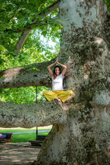 Beautiful woman with gorgeous curly hair doing yoga in nature, dressed in white and yellow combination, concept: active healthy life, in love with nature, support, balance, wellbeing, energy