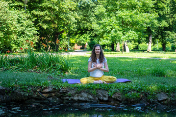 Beautiful woman with gorgeous curly hair doing yoga in nature, dressed in white and yellow combination, concept: active healthy life, in love with nature, support, balance, wellbeing, energy