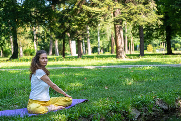Beautiful woman with gorgeous curly hair doing yoga in nature, dressed in white and yellow combination, concept: active healthy life, in love with nature, support, balance, wellbeing, energy