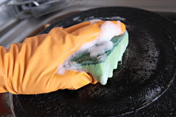 A man's hand in a protective glove cleans a pan with a burnt bottom with a foam kitchen sponge. Up close