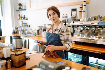 Portrait of friendly waitress at work. Smiling female barista standing behind a bar counter. Business concept, food and drinks
