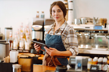 Portrait of friendly waitress at work. Smiling female barista standing behind a bar counter. Business concept, food and drinks