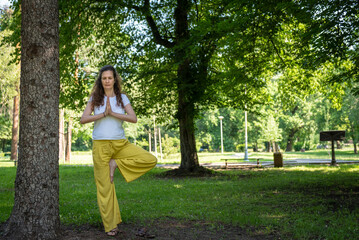Beautiful woman with gorgeous curly hair doing yoga in nature, dressed in white and yellow combination, concept: active healthy life, in love with nature, support, balance, wellbeing, energy