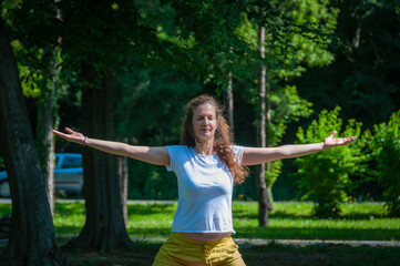 Beautiful woman with gorgeous curly hair doing yoga in nature, dressed in white and yellow combination, concept: active healthy life, in love with nature, support, balance, wellbeing, energy