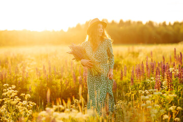 Beautiful woman holding bouquet of lavender flowers walking in summer meadow. Fashion, beauty,...