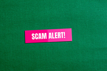 Scam alert words written on pink paper sticker with green background. Conceptual scam alert symbol....