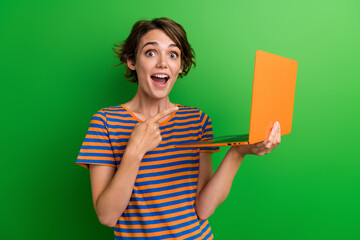 Photo portrait of attractive young woman point excited orange netbook dressed stylish striped clothes isolated on green color background