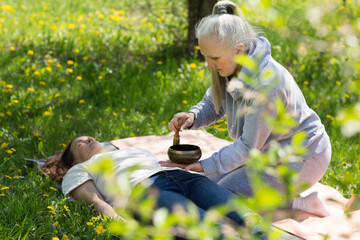 Senior woman doing massage therapy singing bowls in a flowering garden. Sound therapy, recreation,...