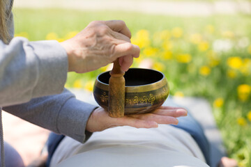 Senior woman doing massage therapy singing bowls in a flowering garden. Sound therapy, recreation,...