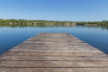 A dock on the lake on the sunny day with nice clean reflection of the forrest behind