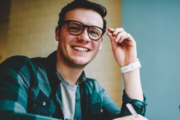 Portrait of cheerful hipster guy in eyewear satisfied with studying in language school doing...