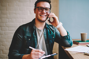 Portrait of cheerful man satisfied with telephone consultancy while noting information for...