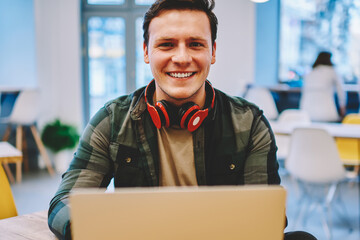Portrait of cheerful hipster guy with headphones enjoying studying online language course on...