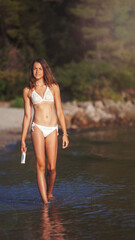 Obraz premium Cute girl walking through the sea water and holding sunlotion