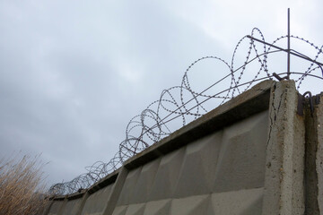 Barbed wire over a concrete wall against the background of a cloudy sky