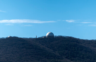 White dome of the observatory on a mountain in the forest against the sky