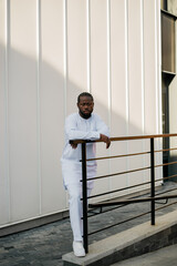 Cheerful male tourist dress in white wear dashiki ethnic smiling at city street on stairs. African American travel model have free time. Copy space