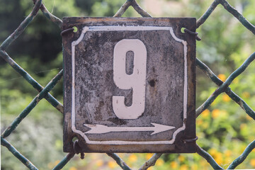 Weathered grunge square metal enameled plate of number of street address with number 9