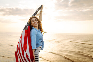 Cheerful happy woman outdoors on the beach holding USA flag having fun. USA celebrate 4th of July....