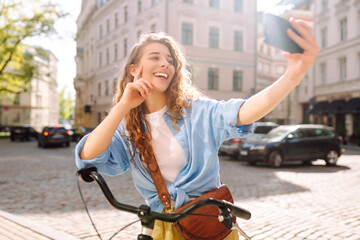 Young woman using mobile phone while  riding bicycle at the city street outdoor....