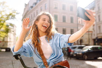 Young woman using mobile phone while  riding bicycle at the city street outdoor....