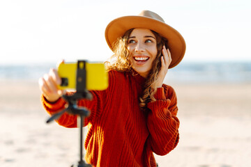 Style woman using smartphone with stabilizer, taking pictures and live video on the seashore....