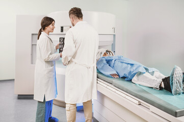 two doctors and a patient in the MRI room. Male doctor and female assistant preparing adult female...