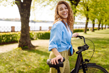 Young smiling woman riding bicycle bike on sidewalk in city spring park outdoors. Active urban...