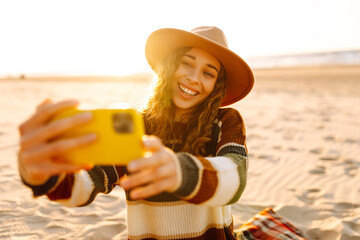 Selfie time. Beautiful curly woman posing by the sea at sunset. Spring time.Travel, weekend, relax and lifestyle concept.