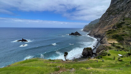 A stunning coastal view in Madeira, with rocky cliffs, crashing waves, and lush green hills meeting the Atlantic Ocean
