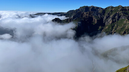 A stunning view of Madeira’s mountains emerging through a sea of clouds, with a bright blue sky and rugged peaks