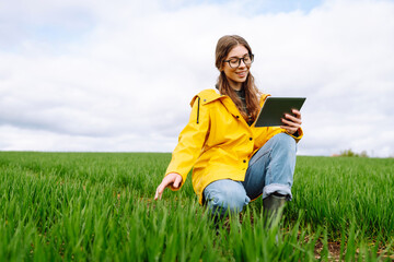 Woman Farmer on a green wheat field with a tablet. Smart farm. The concept of the agricultural...