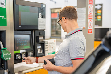 The man pays for fuel with a credit card on terminal of self-service filling station in Europe