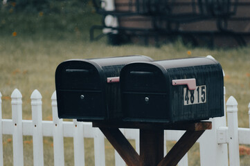 Close-up of mailboxes on a post in front of a white fence