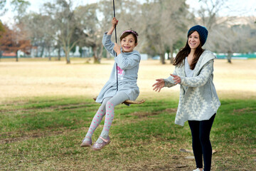 Mother, portrait or child on swing in park on holiday or vacation in winter with freedom in games. Kid, playground or mom with happy girl, support or push for outdoor bonding together with fun moment