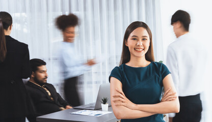 Young Asian businesswoman portrait poses confidently with diverse coworkers in busy meeting room in...