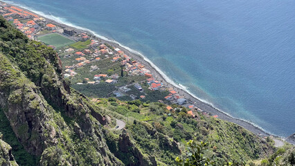 Aerial view of a coastal village on Madeira Island, nestled between steep cliffs and the blue Atlantic Ocean