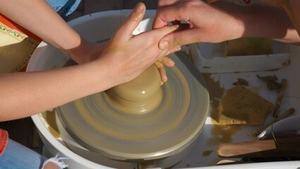 Making pot next clay wheel. A view of couple hands making a clay pot on the wheel in the sun during day time.