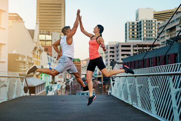 High five, runner or happy people jump for fitness training, exercise or workout success on outdoor bridge. City, excited or sports athletes with friends or teamwork for running on urban street road
