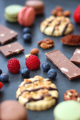Macarons, chocolate, cookies, berries and various nuts on dark blue background. Selective focus.