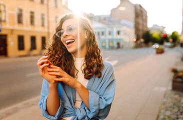 Fototapeta premium Fashionable young woman in good mood posing outdoors. Sunny day. Concept of lifestyle, fashion, travel.