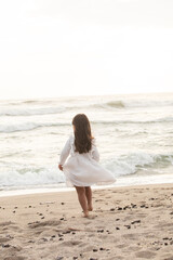 Fototapeta na wymiar Little girl with white dress running in the beach during sunset in Lima Peru 