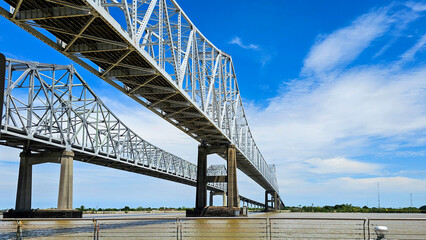 The Crescent City Connection bridge over the Mississippi River with lush green trees and plants, blue sky and clouds in New Orleans Louisiana USA