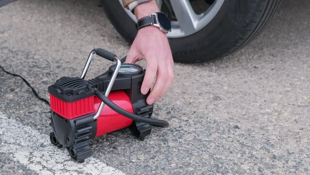 A man turns on a car air compressor to inflate tires.