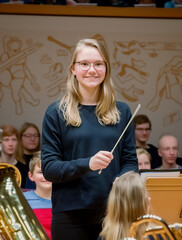 A teenager conductor girl leads with intensity and passion during a concert, using a baton in a well-lit room