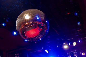 Classic large disco ball made of small mirrors reflecting bright and warm lights on the ceiling of...