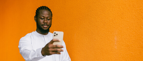 Banner Happy young African American man in dashiki ethnic clothes taking selfie on orange wall...