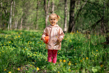 A little girl of 2-3 years old stays in the forest and enjoys nature. Background of a green forest. She is joyful and dreamy.