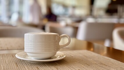 A coffee cup is placed on a saucer, resting on a wooden table. The tableware includes dishware and...